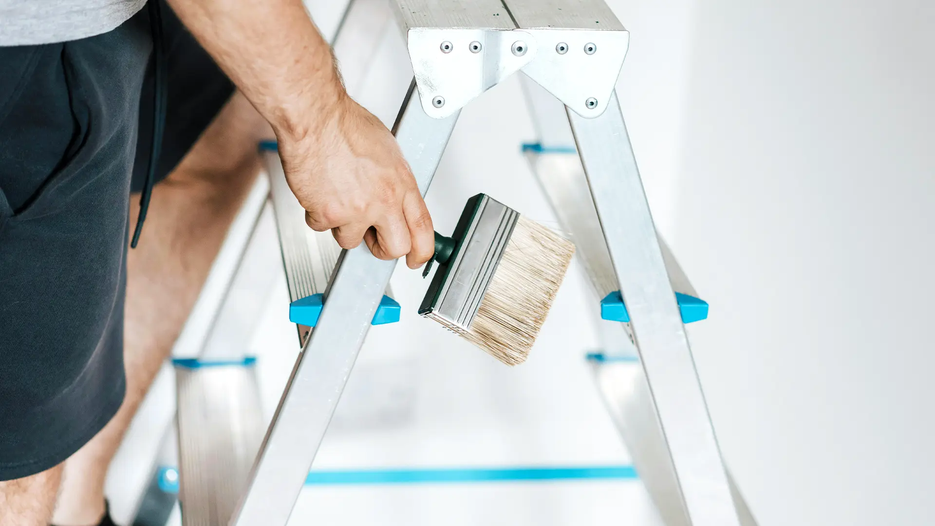 Male hand holding a paint brush while standing on a ladder